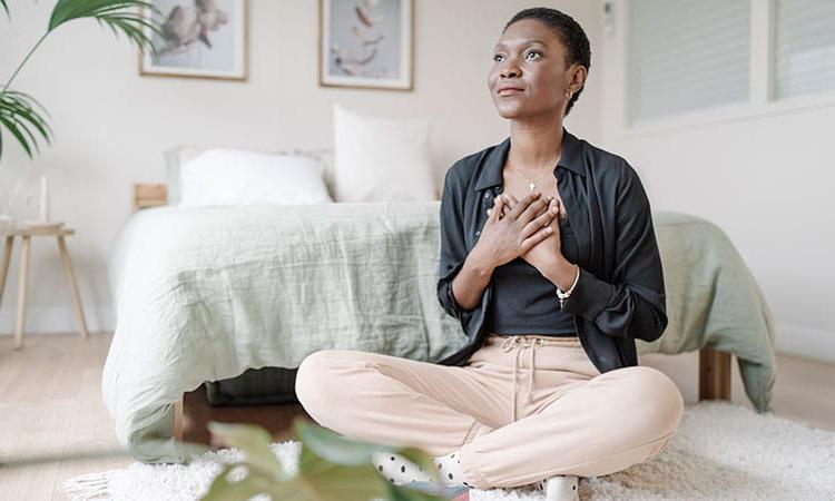 Woman with h和s on her chest sitting on the floor in her bedroom in 冥想.