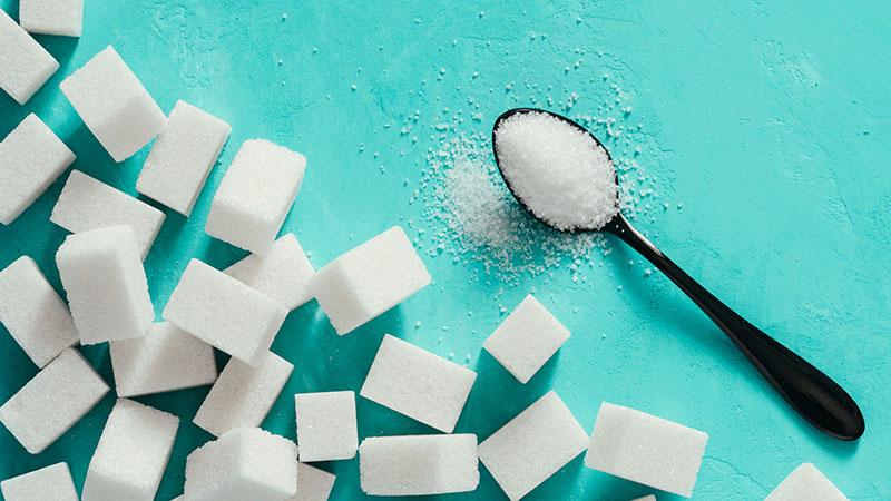 Sugar cubes and sugar in spoon. White sugar on turquoise background