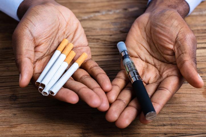 man holding a vape pen and cigarettes