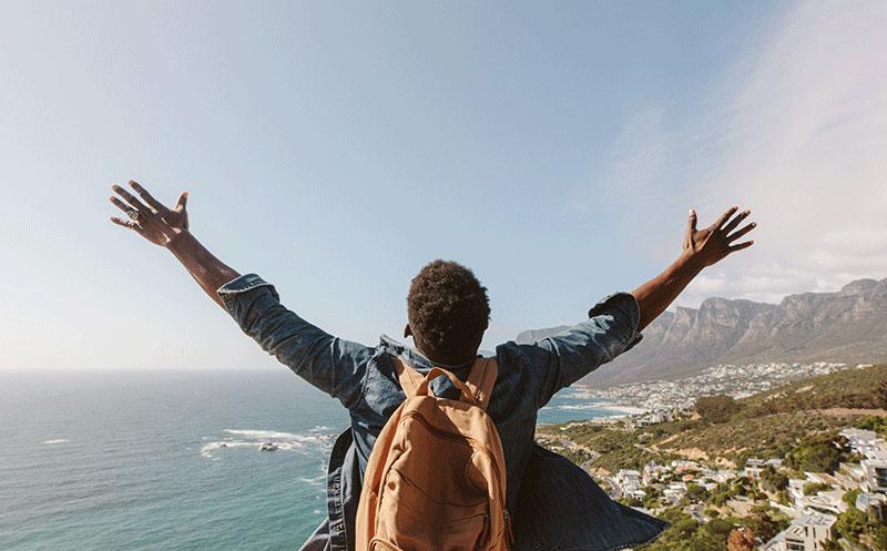 back of man with backpack raising arms in success